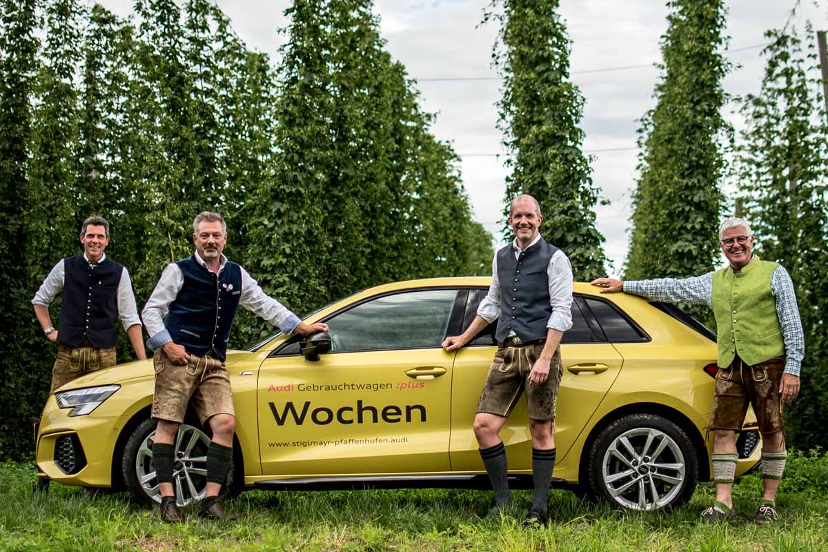 Unsere drei Audi Gebrauchtwagenverkäufer stehen mit dem Verkaufsleiter in Tracht vor einem Audi im Hopfengarten
