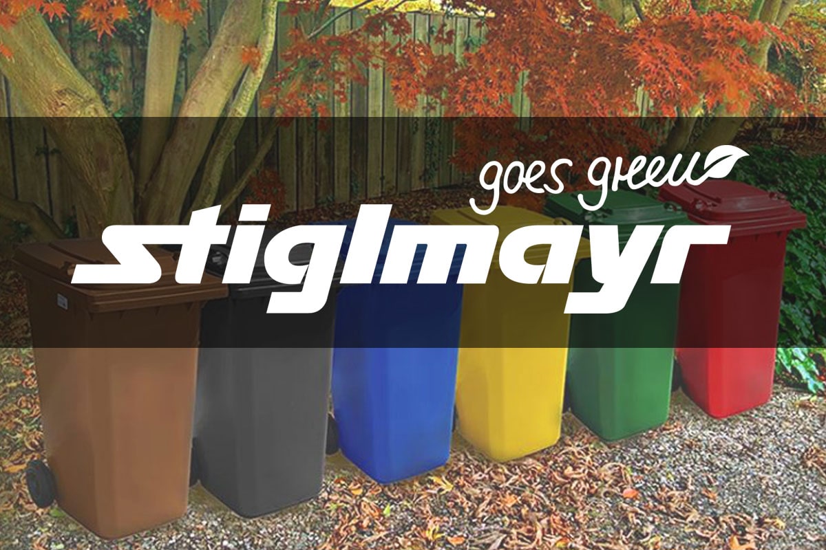 Bild zeigt das Logo Stiglmayr goes green. Im Hintergrund stehen Mülltonnen in verschiedenen Farben, welche die Mülltrennung Symbolisieren sollen.