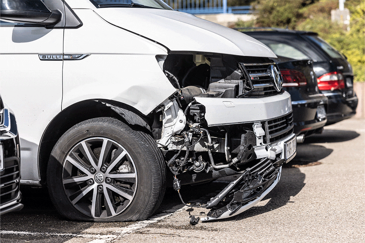 Ein weißes Fahrzeug mit kaputter Front steht neben weiteren Autos.