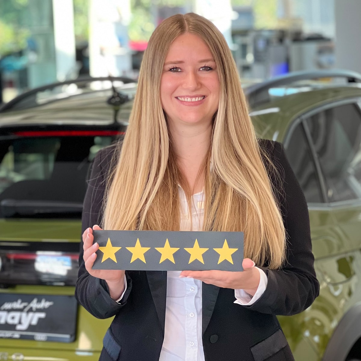 Neuwagen Verkäuferin Amelie Magg lächelt in die Kamera und hält ein Schild mit fünf Sternen in der Hand