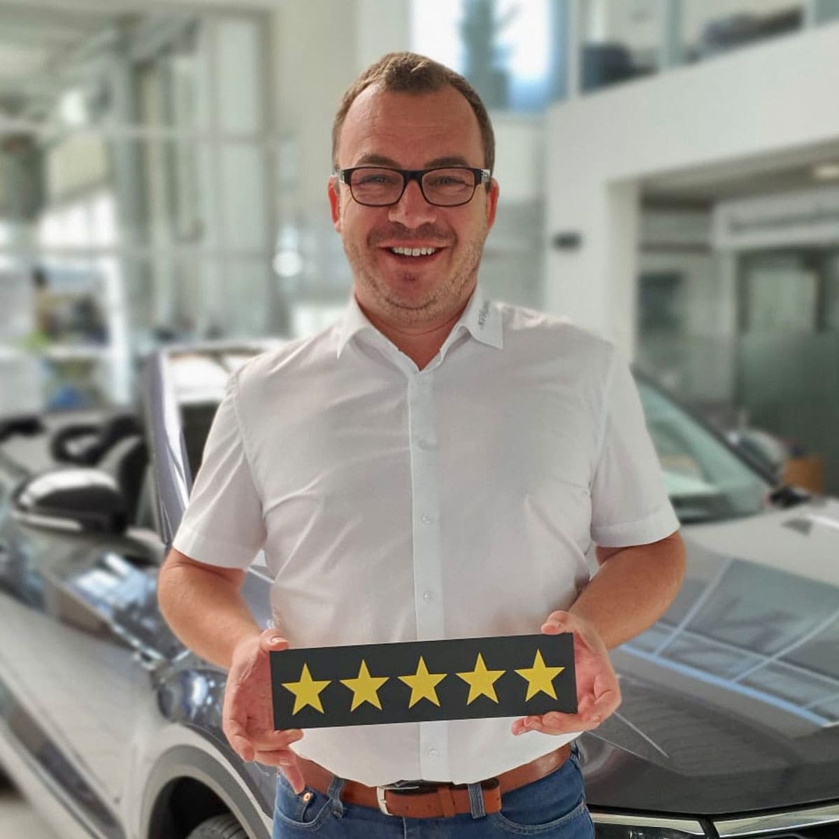 Mitarbeiter Bernd Schreier lächelt in die Kamera und hält ein Schild mit fünf Strenen in der Hand