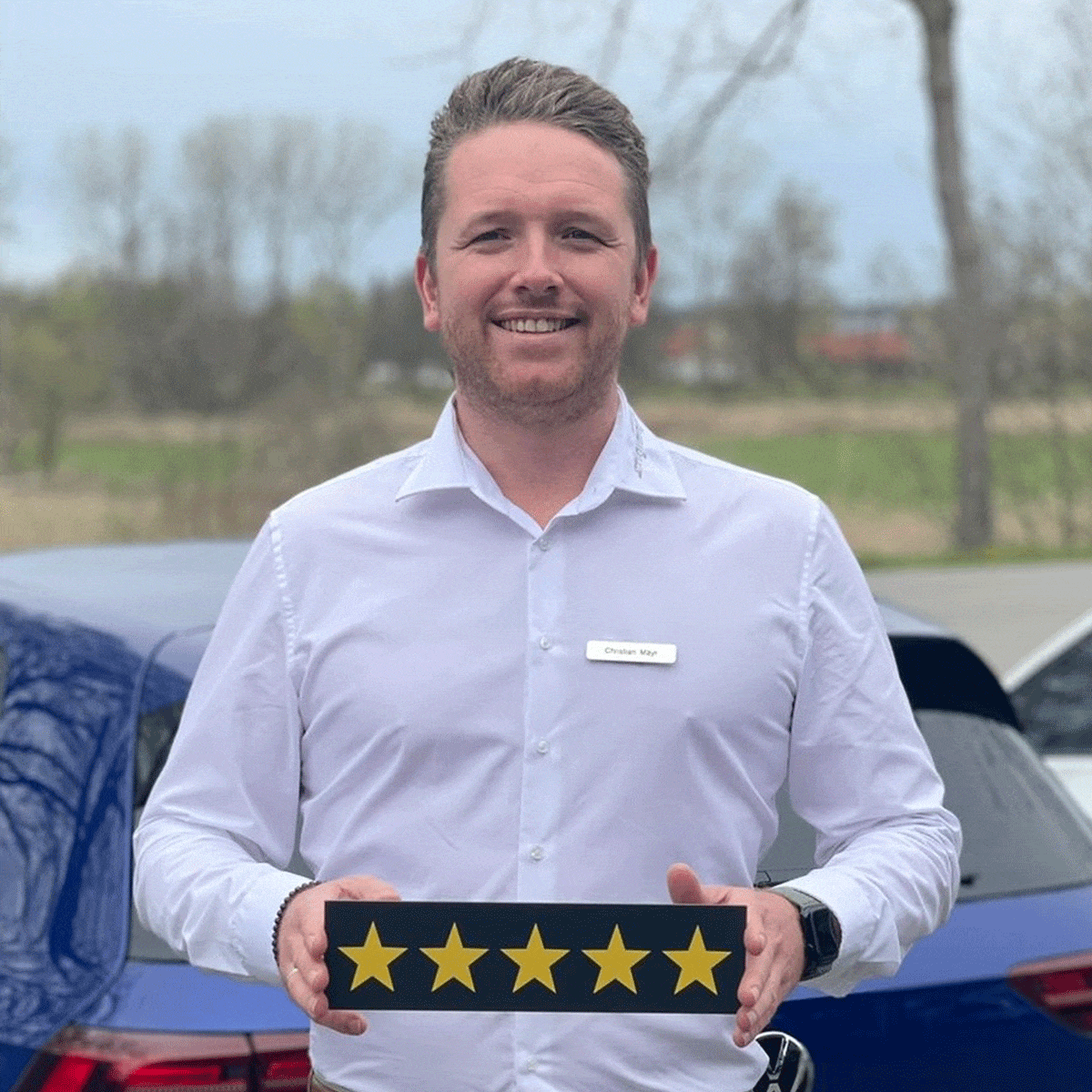 Verkäufer Christian Mayr lächelt in die Kamera und hält ein Schild mit fünf Sternen in der Hand