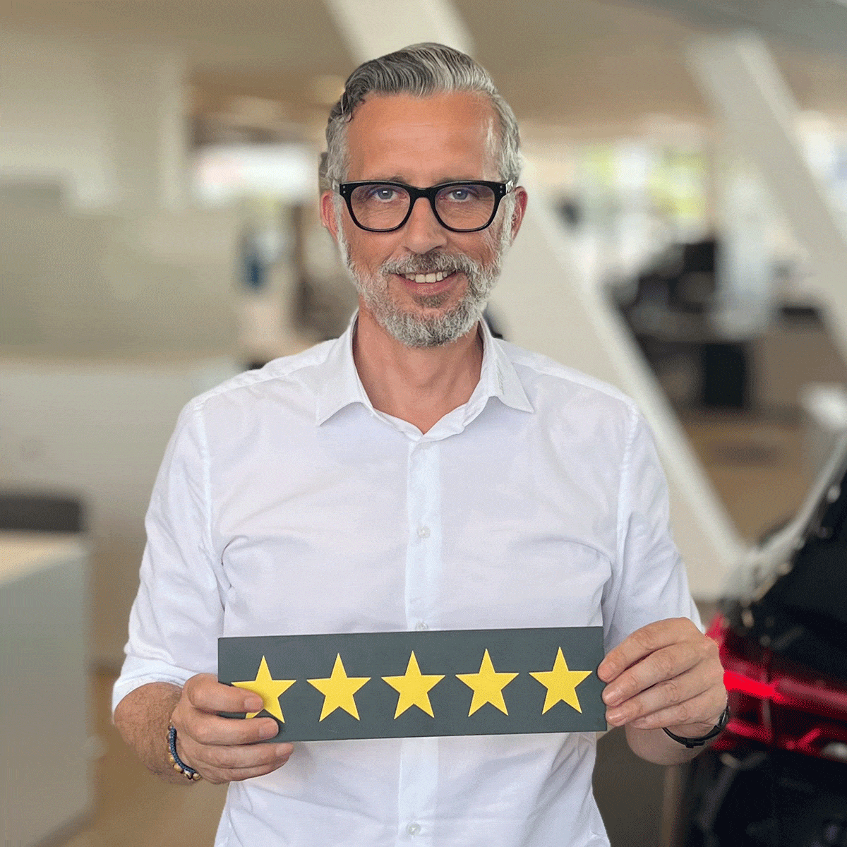Neuwagen Verkäufer Dirk Hochbaum lächelt in die Kamera, und hält ein Schild mit fünf Sternen in der Hand