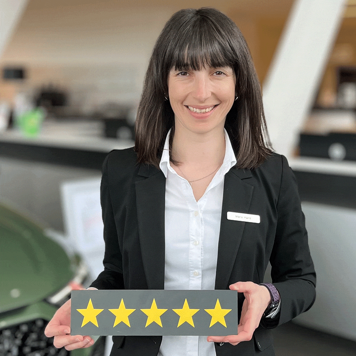 Serviceleitung Maria Hainz lächelt in die Kamera und hält ein Schild mit fünf Sternen in der Hand