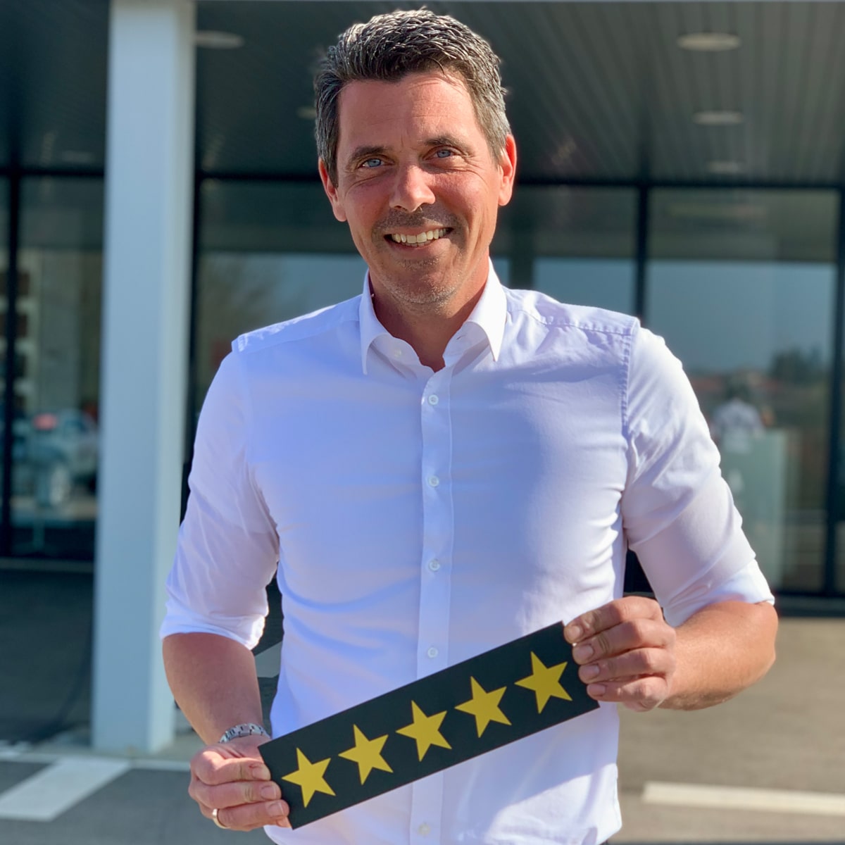 Gebrauchtwagenverkäufer Martin Grandl lächelt in die Kamera und hält ein Schild mit fünf Sternen in der Hand