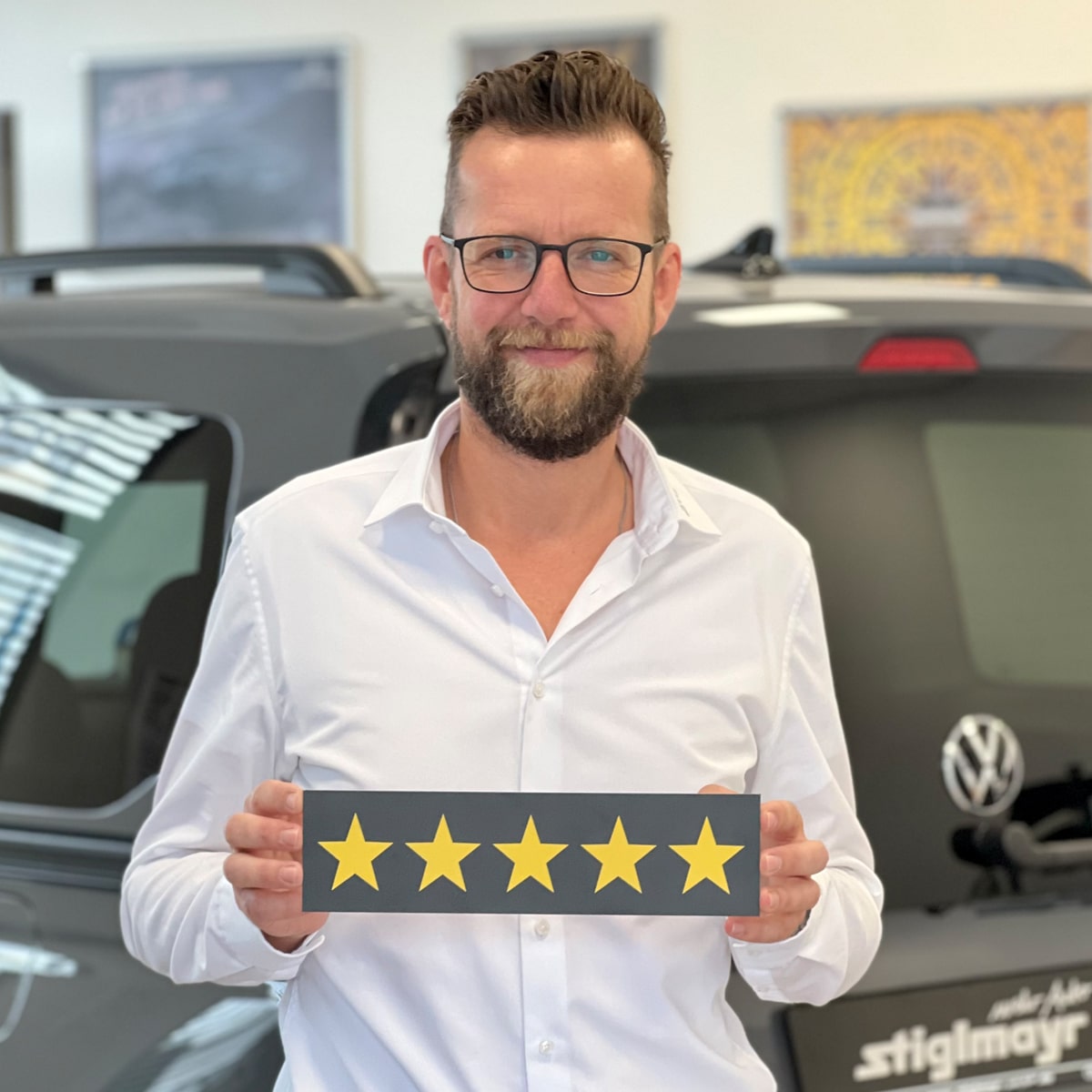 Verkäufer für Nutzfahrzeuge Oliver Schroeder lächelt in die Kamera und hält ein Schild mit fünf Sternen in der Hand
