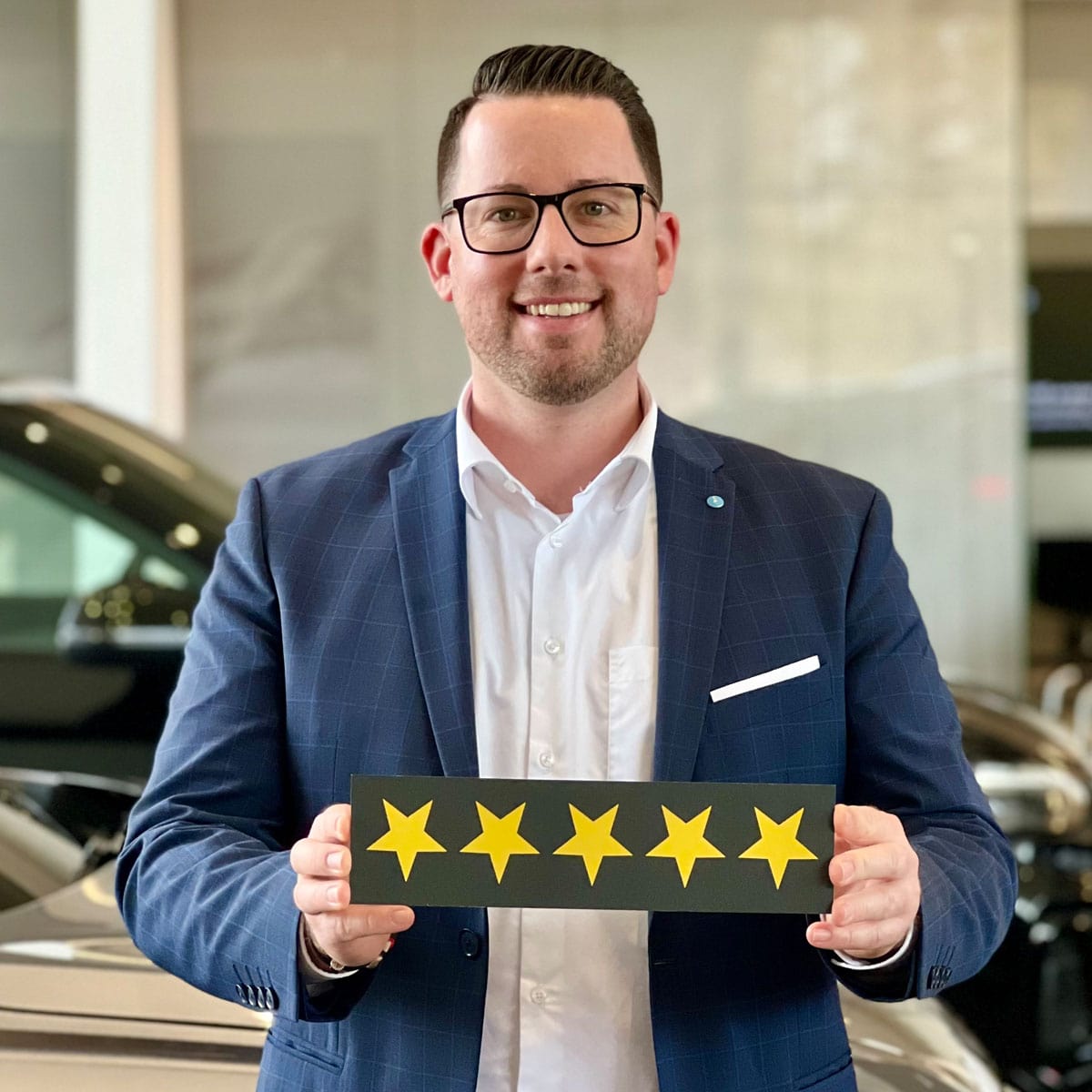 Neuwagen Verkäufer Sebastian Sander lächelt in die Kamera und hält ein Schild mit fünf Sternen in der Hand