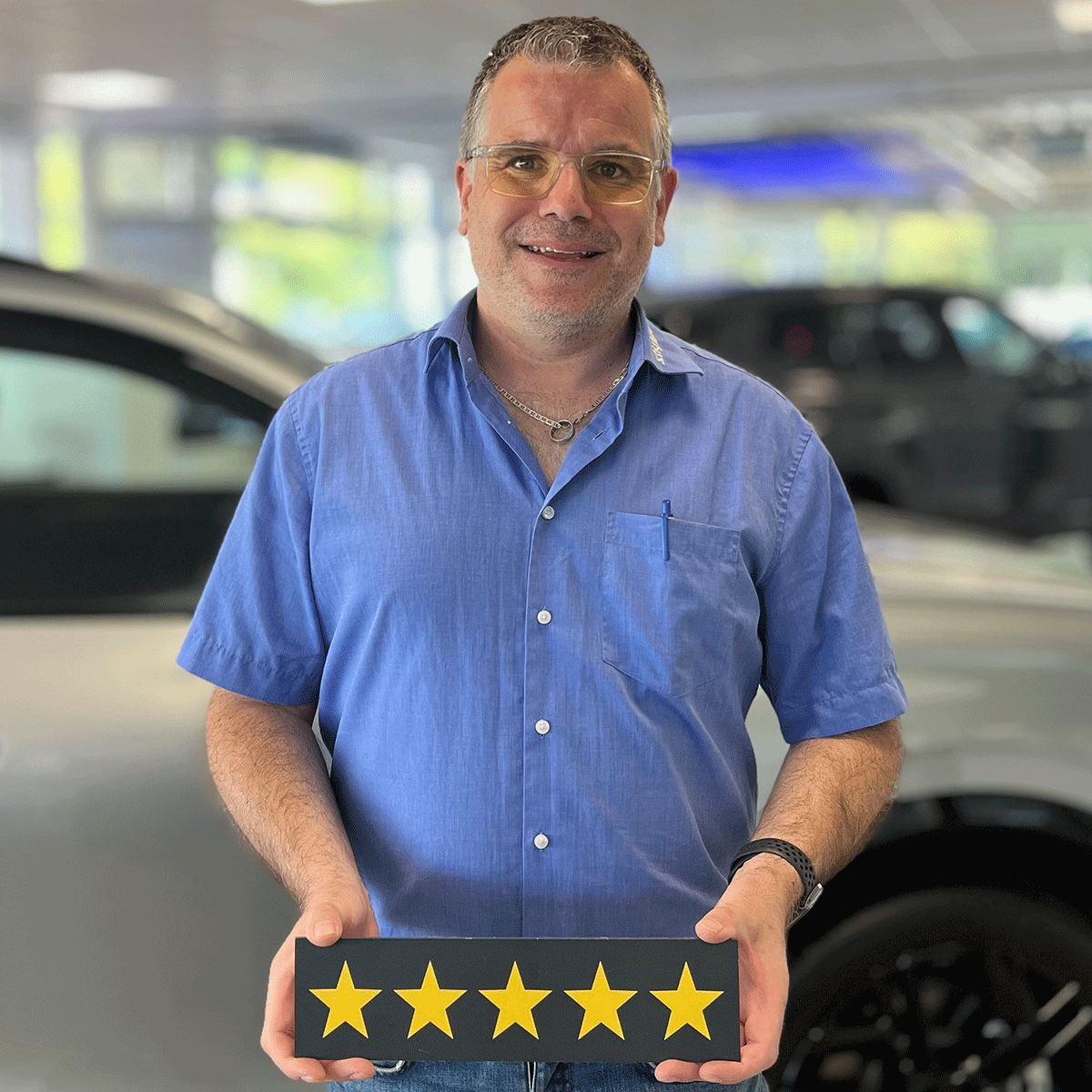 Serviceberater VW Betrieb Benjamin Herrmann lächelt in die Kamera und hält ein Schild mit fünf Sternen in der Hand.