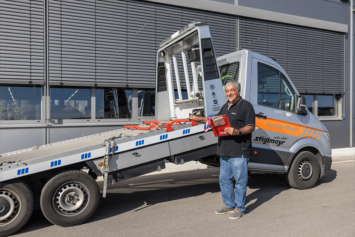 Ein Mitarbeiter steht vor einem Abschleppwagen mit einer roten Klemmmappe in der Hand.