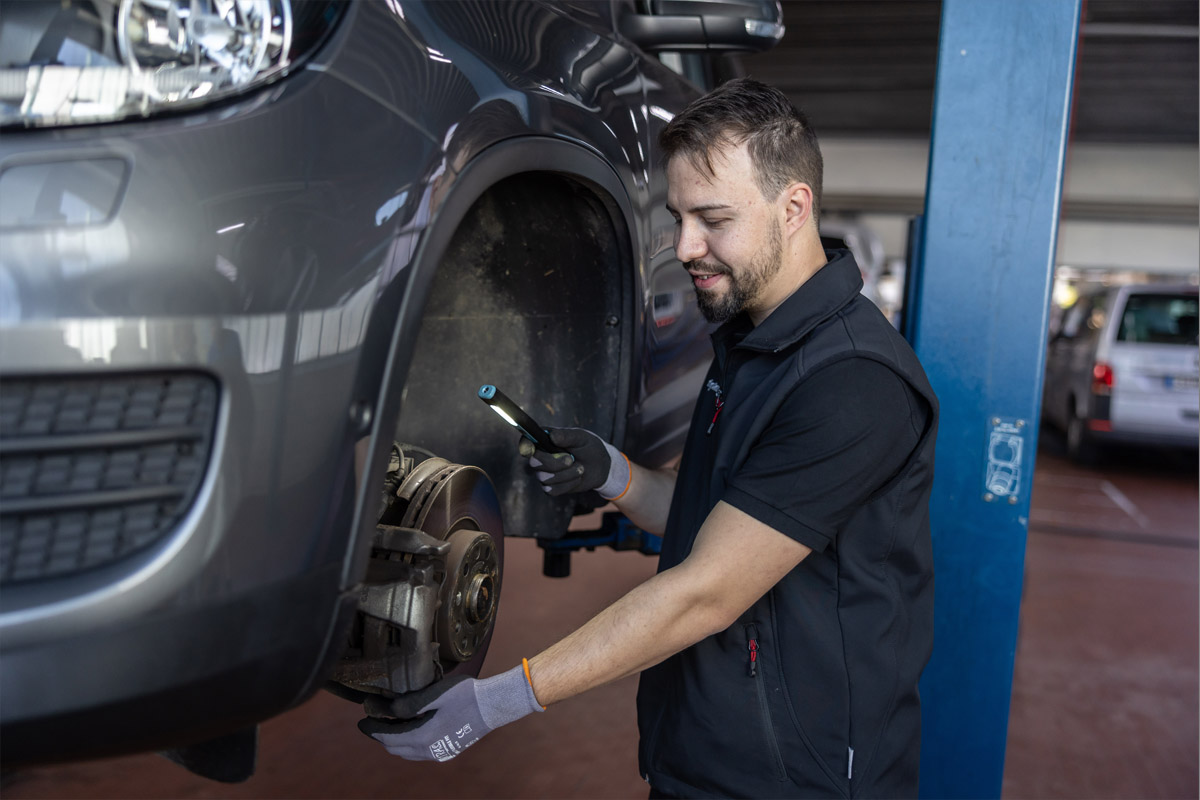 Mechatroniker steht in der Werkstatt und schaut sich etwas an dem Fahrzeug an.